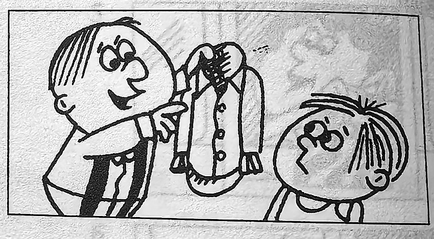A boy points to a shirt he is holding.
