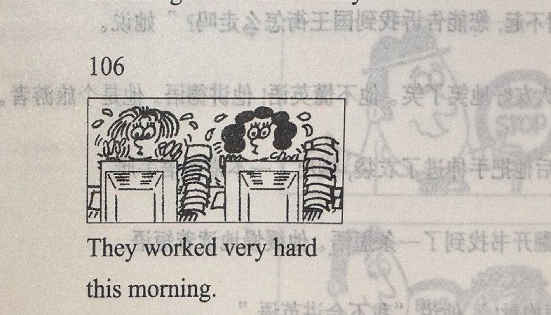 Two people work very hard at a desk, surrounded by stacks of papers.